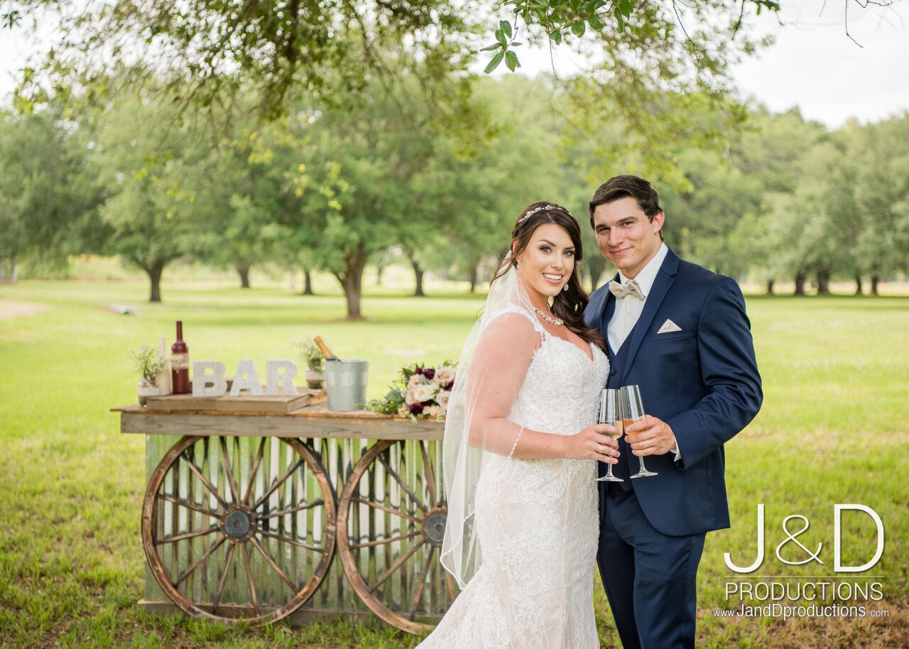 A bride and groom pose for a picture in front of an old wagon.