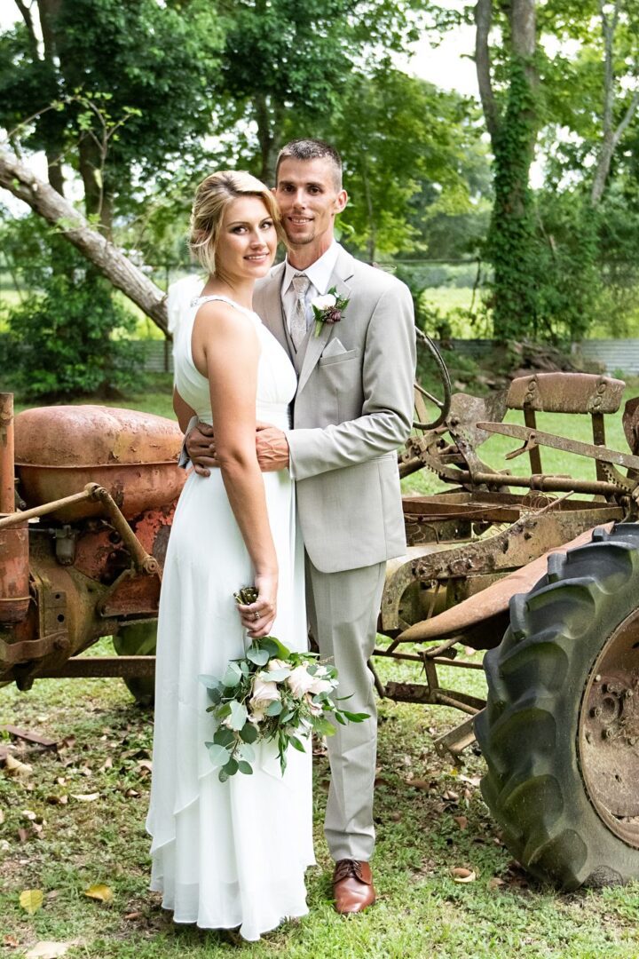 A man and woman posing for a picture in front of an old tractor.