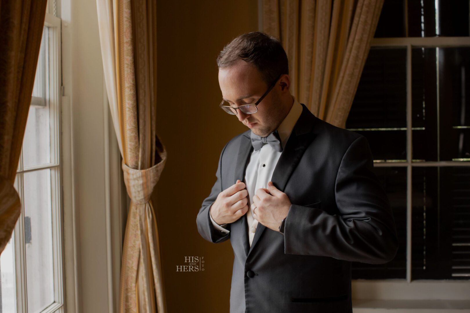 A man in a suit and bow tie fixing his collar.