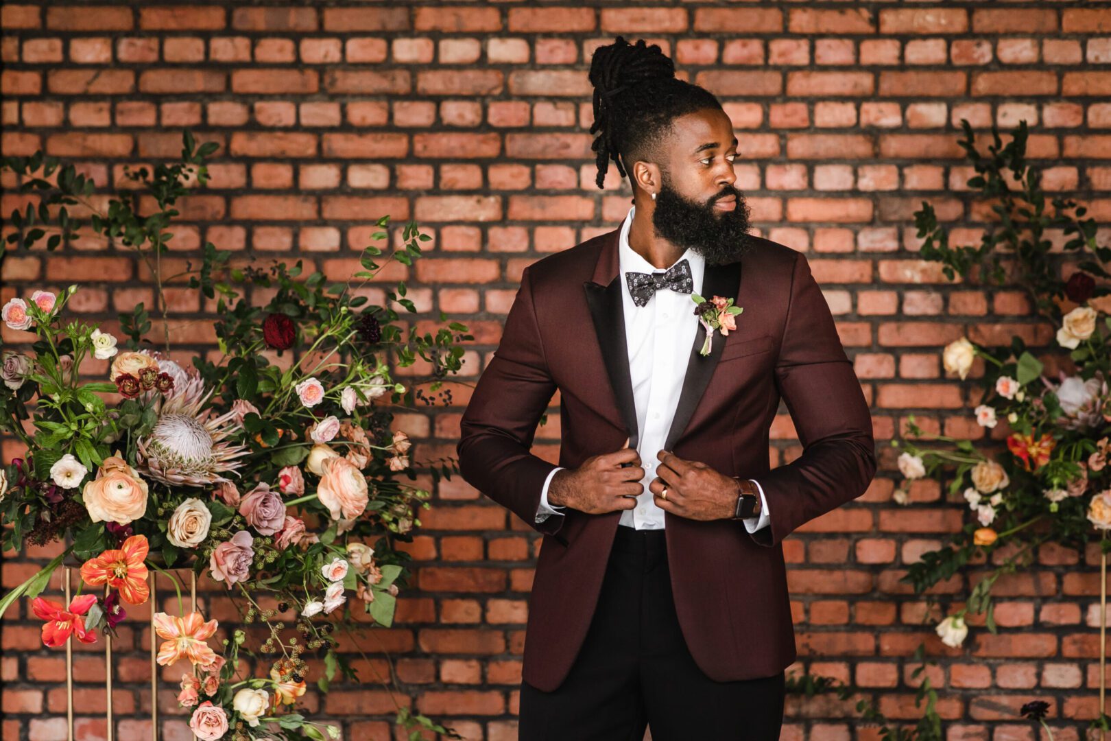 A man in a suit and bow tie standing next to flowers.