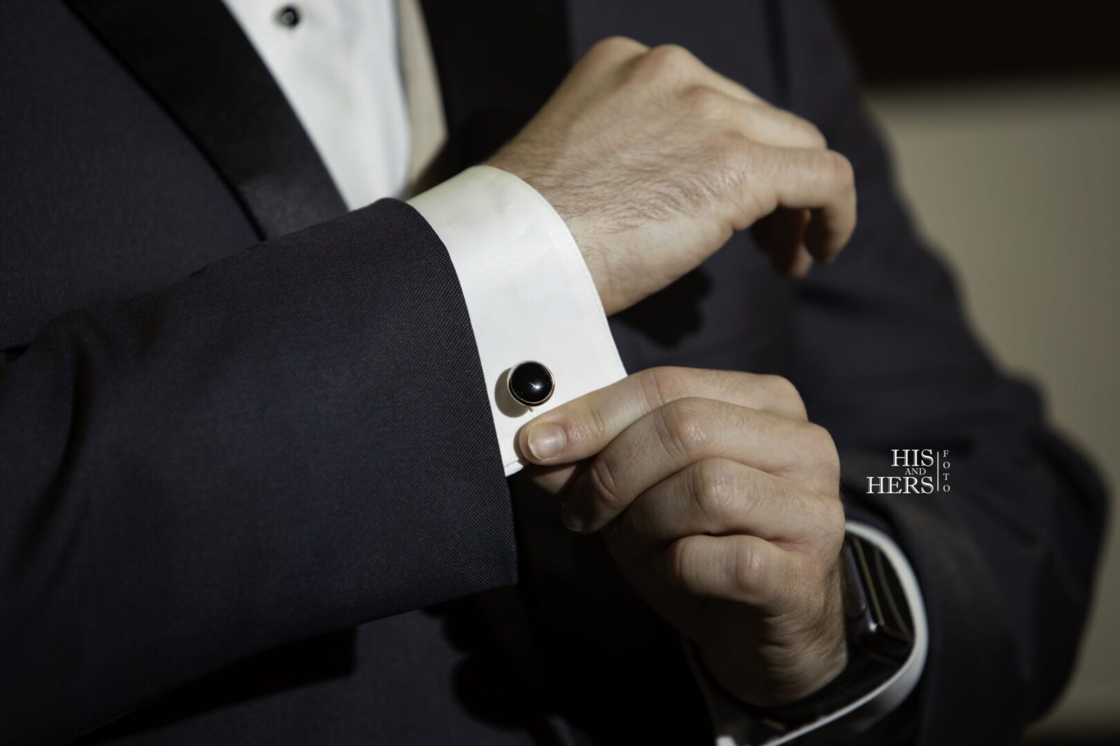 A man in a tuxedo adjusting his cuff.