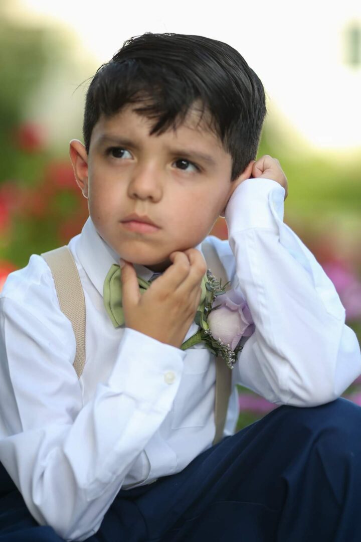 A young boy in white shirt and tie holding his hand to the side of his face.