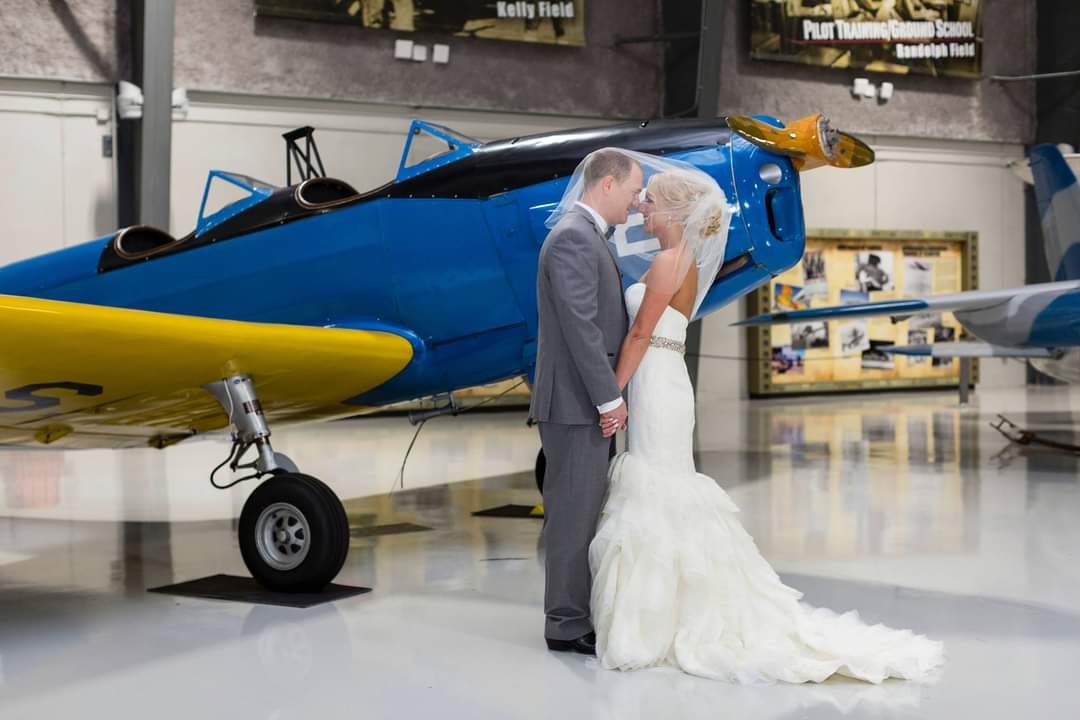 A bride and groom kissing in front of an airplane.