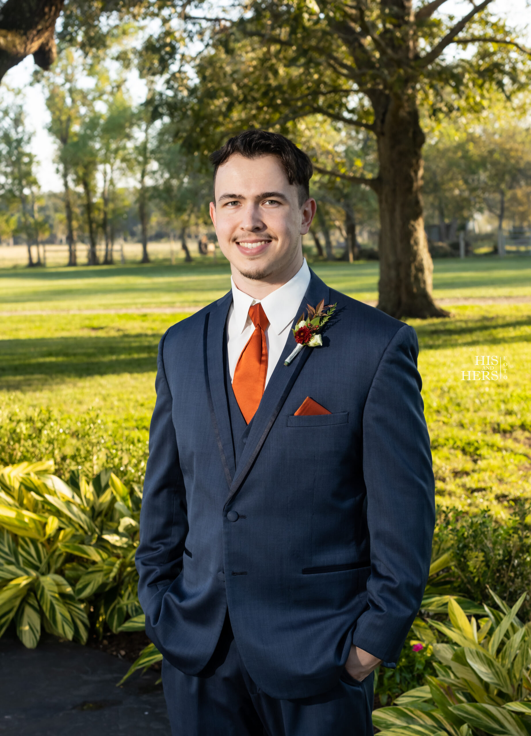 A man in a suit and tie standing next to a tree.