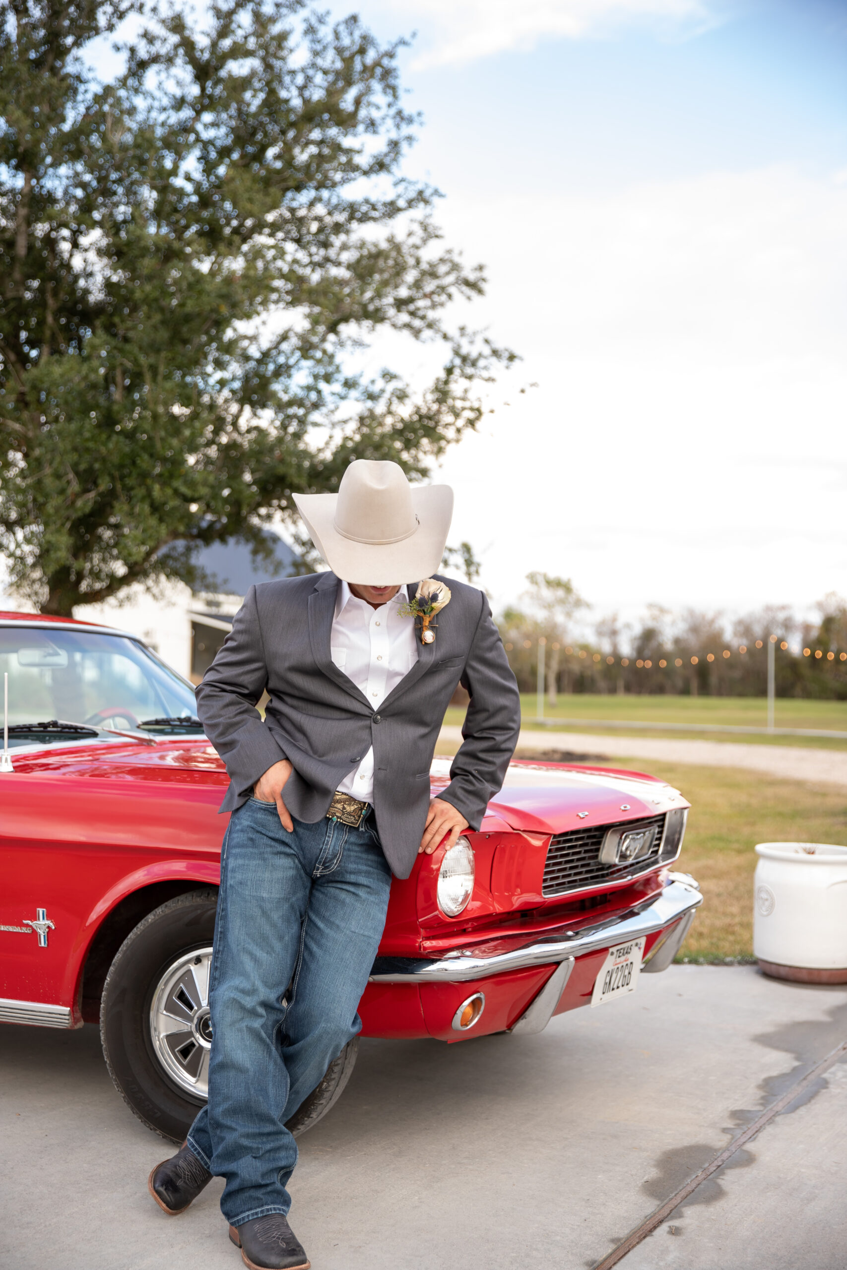 A man in cowboy hat leaning on the hood of a red car.